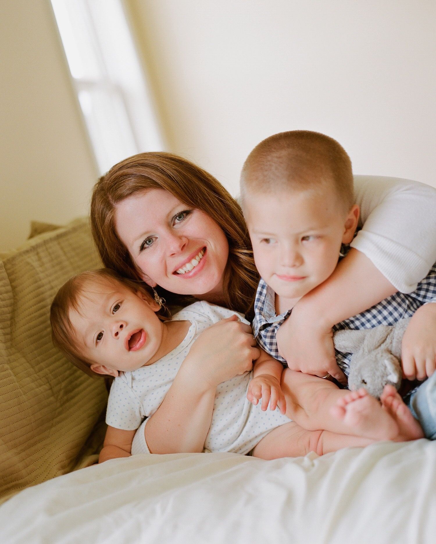 Sweet candid moment of family members cuddling together on white bedding.