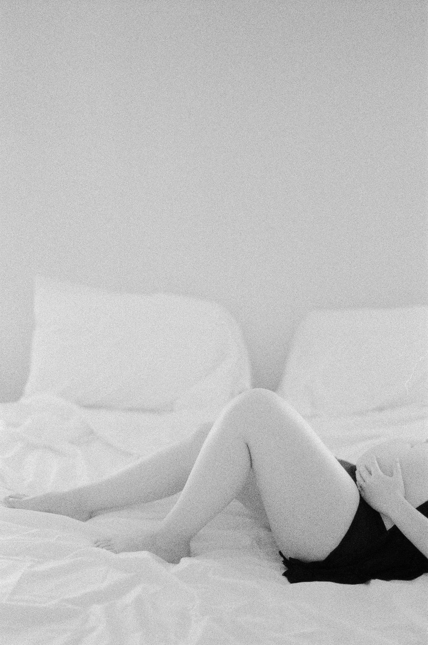 Minimalist black and white boudoir photography with soft curves and white bedding.