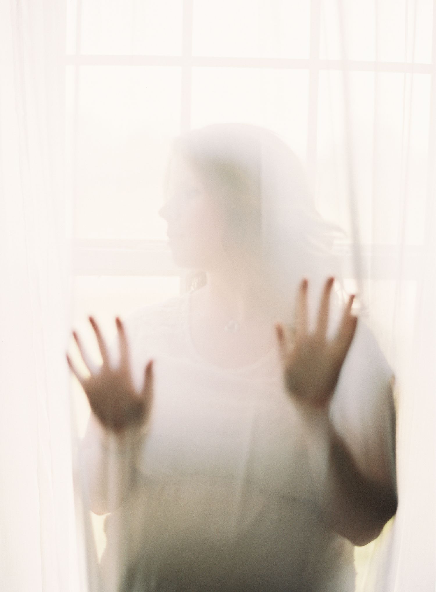 Silhouette of hands pressed against a white translucent curtain creating a ghostly effect.