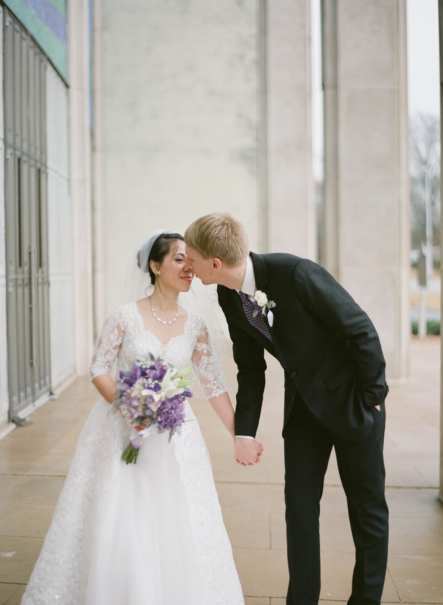Wedding couple sharing playful moments in formal attire against white columns.