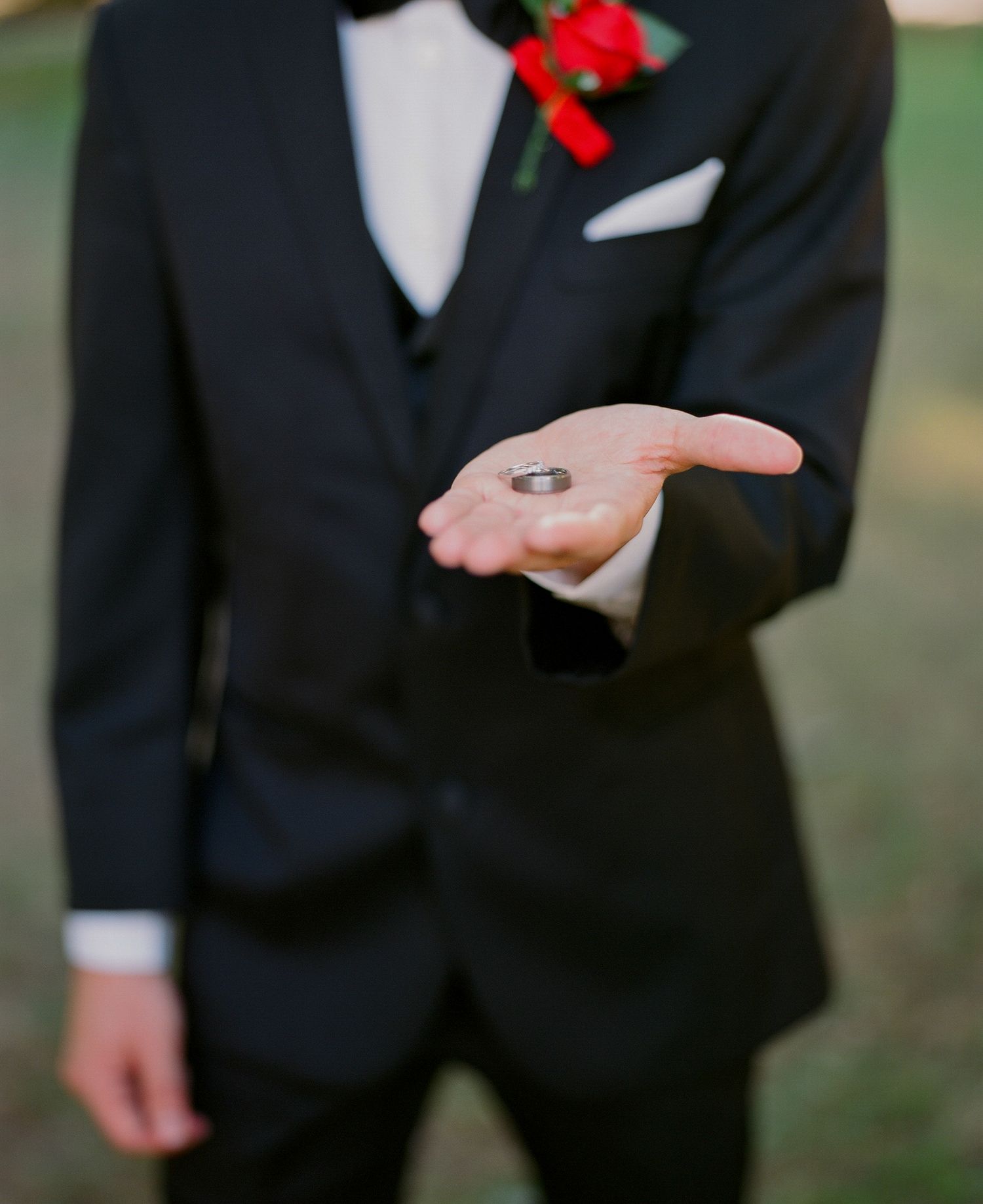 Groomsmen in black tuxedos with red boutonnieres stand together outdoors.