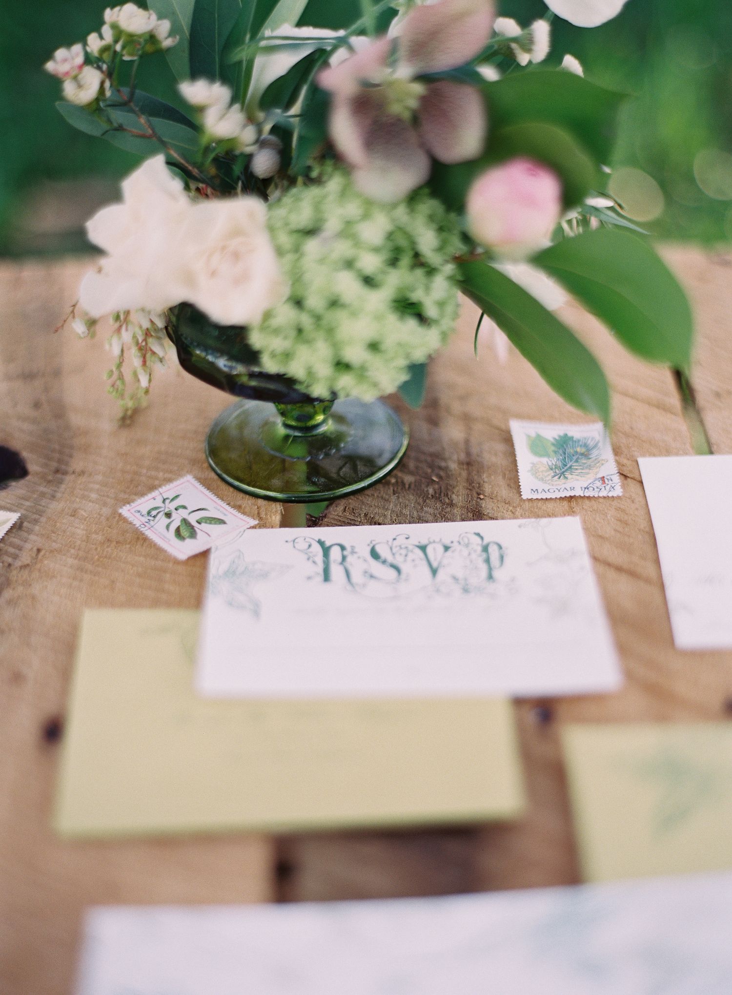 Wedding stationery and RSVP cards arranged with delicate flowers on wooden surface.