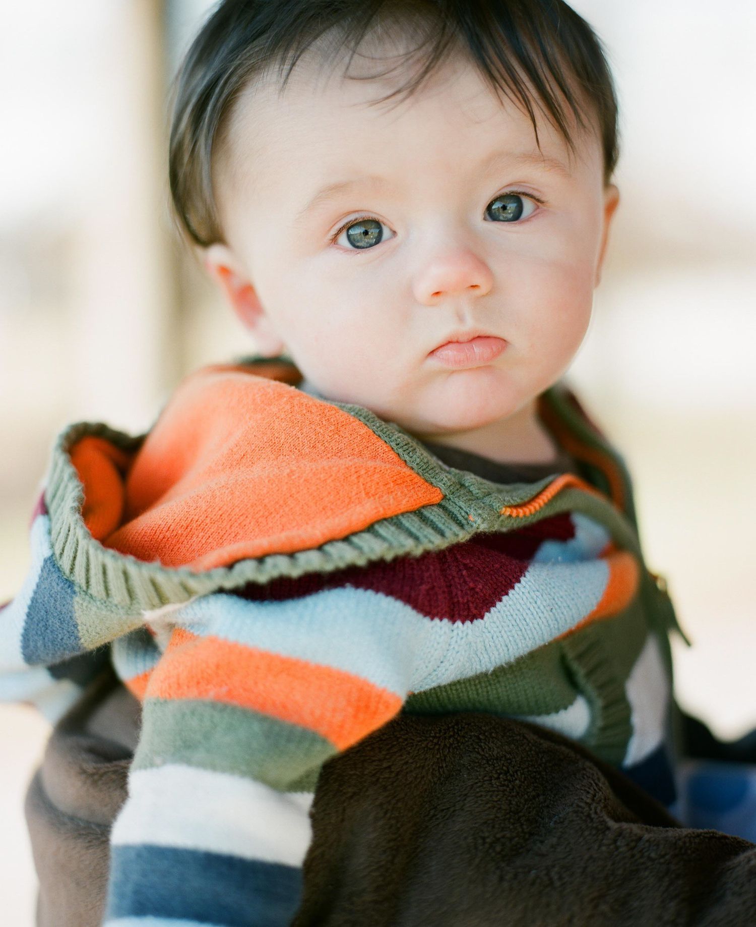 Baby wearing a colorful striped sweater in orange, grey and burgundy tones.