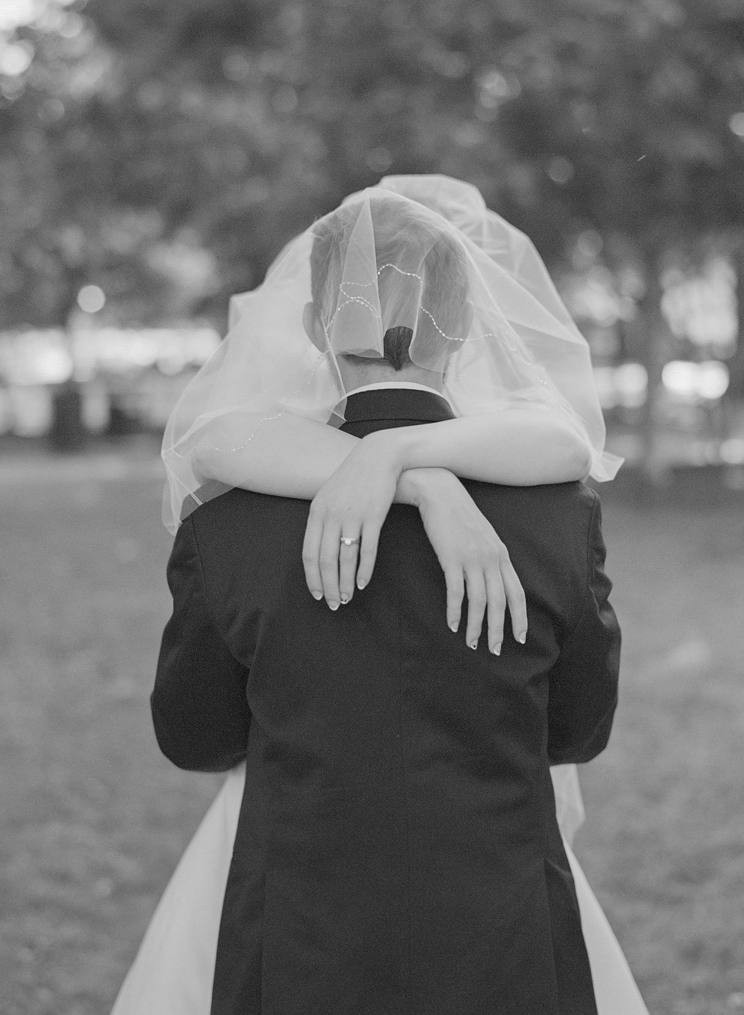 Artistic black and white wedding photo focusing on bride's hands on groom's back.