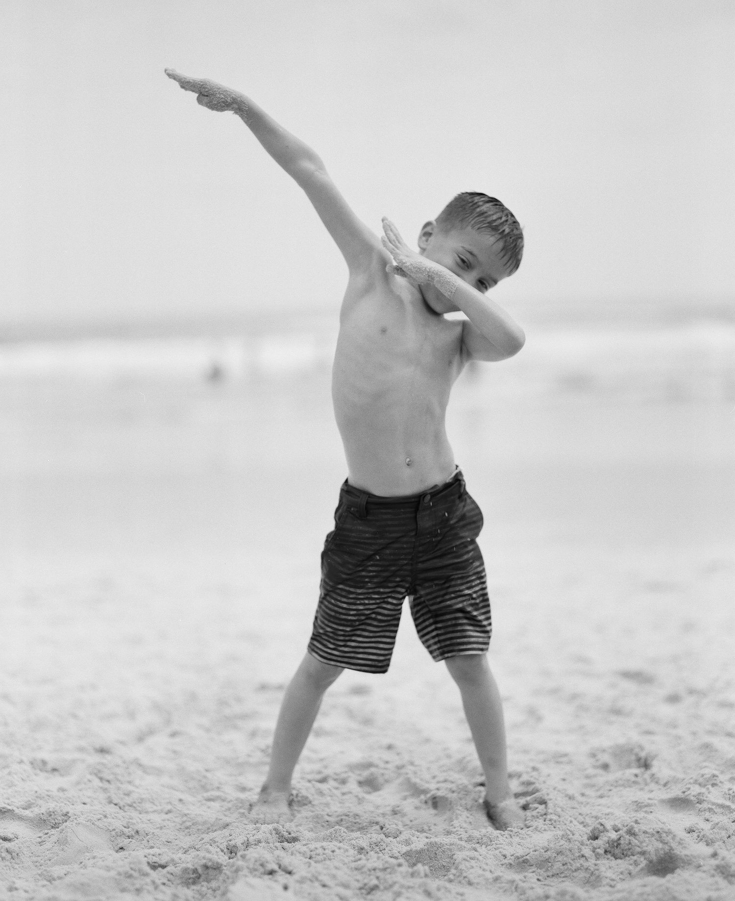 Child making dynamic poses while playing in beach sand.