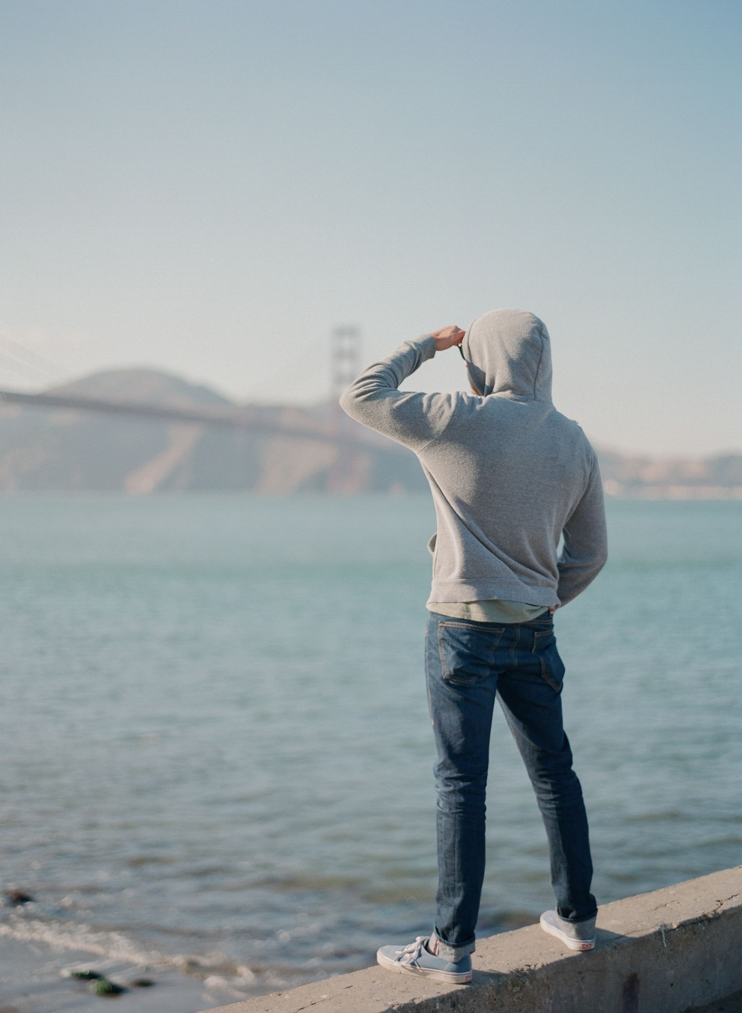 Person bending down at edge of waterfront with mountains visible in background.