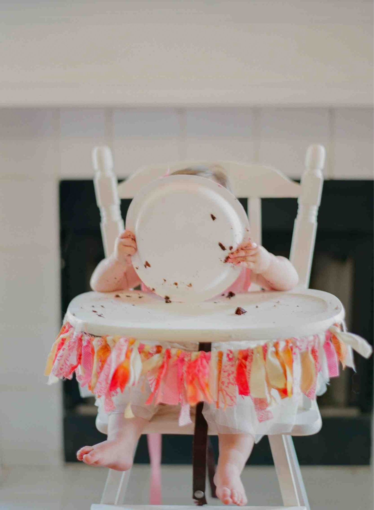 White high chair decorated with pink and coral fabric garland for a special celebration.