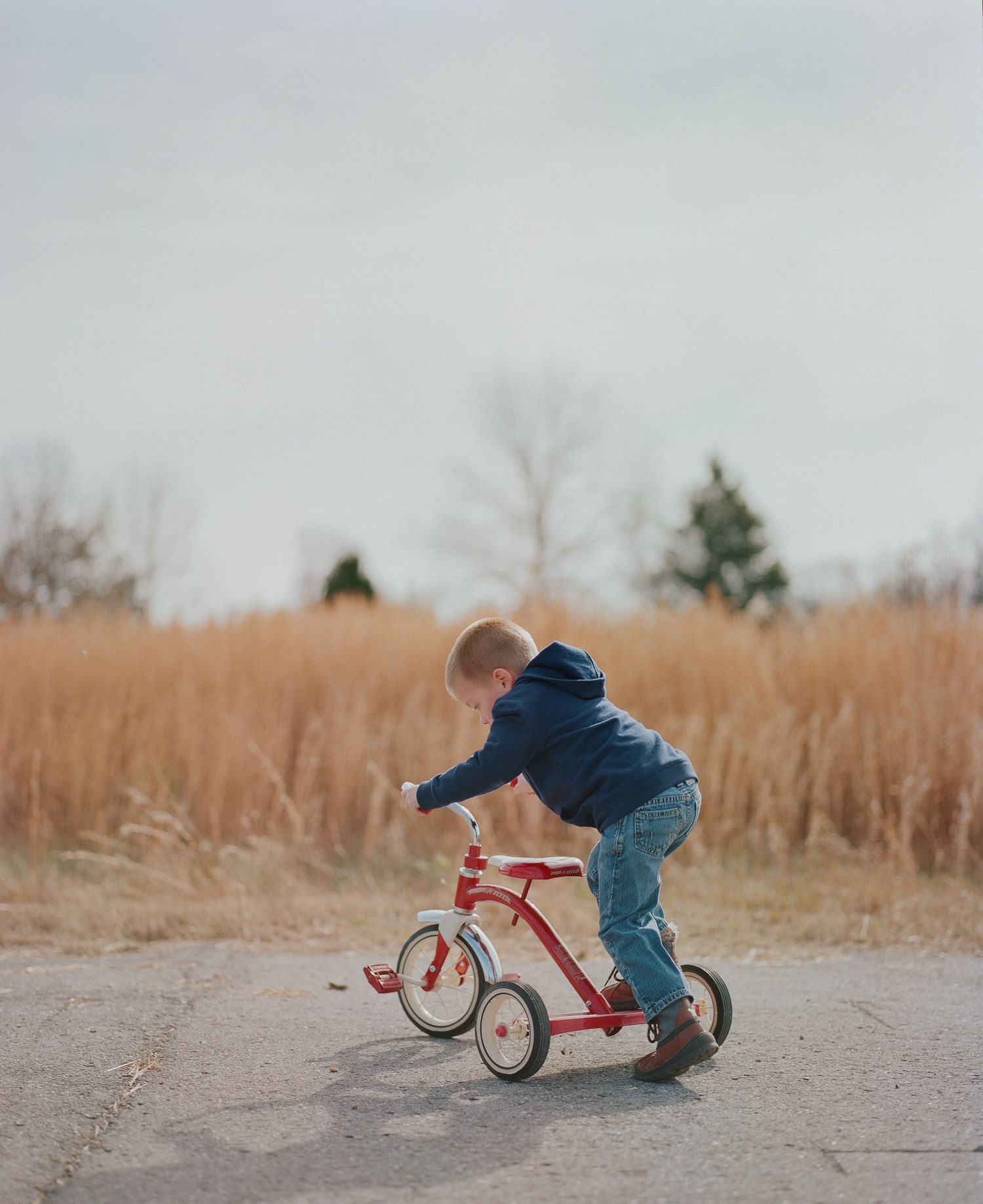 Child falling off red tricycle in sequence of action shots on dirt path.