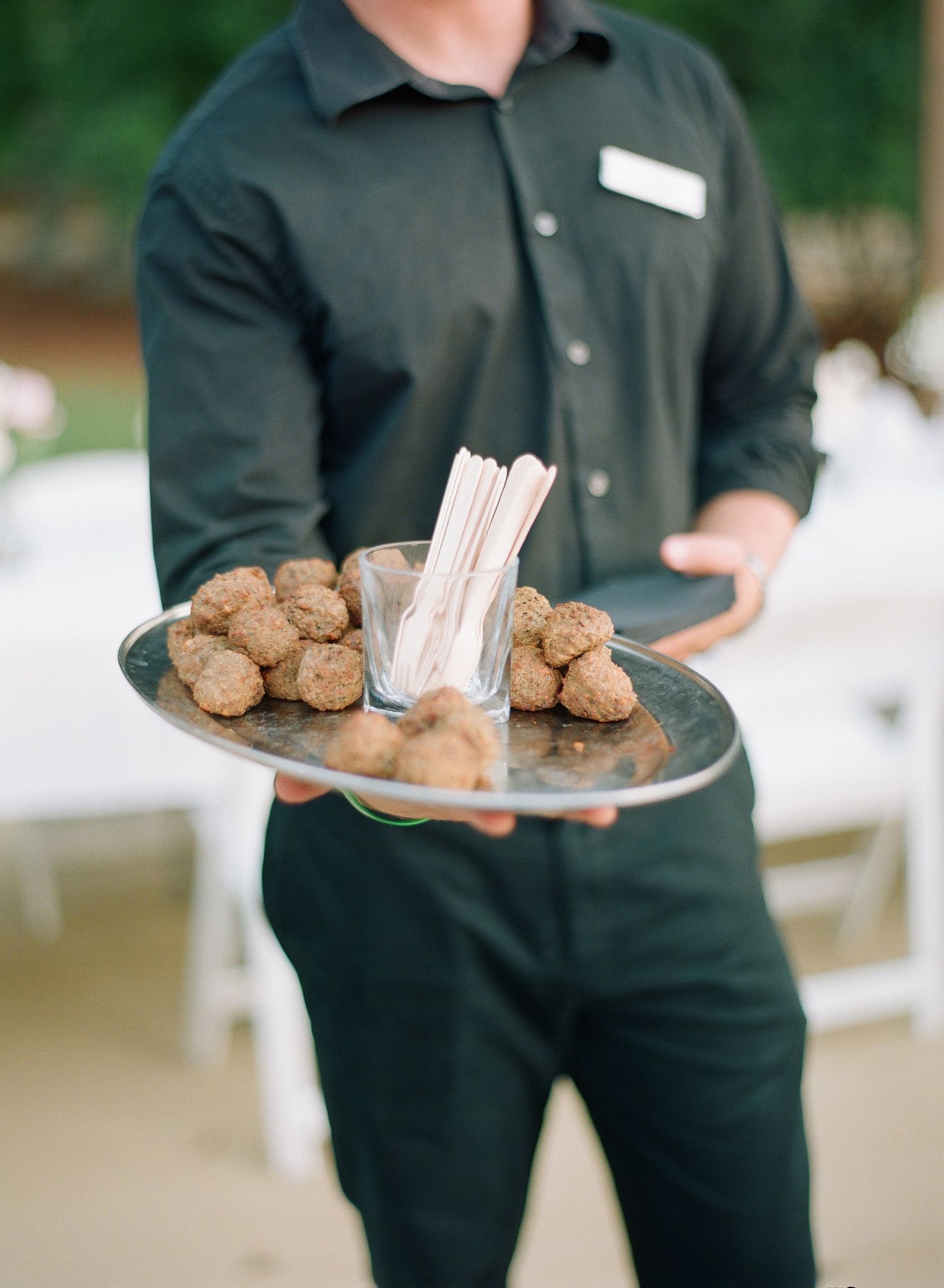 Server carrying plates of cookies and napkins at an outdoor event.