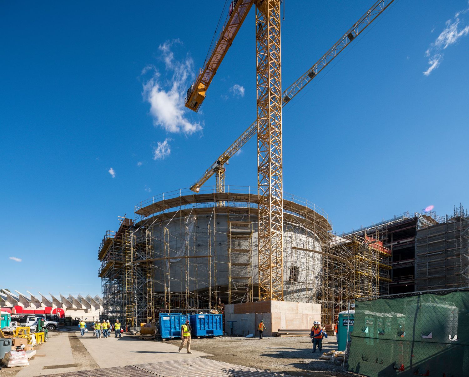 Construction site with scaffolding and cranes against clear blue sky.
