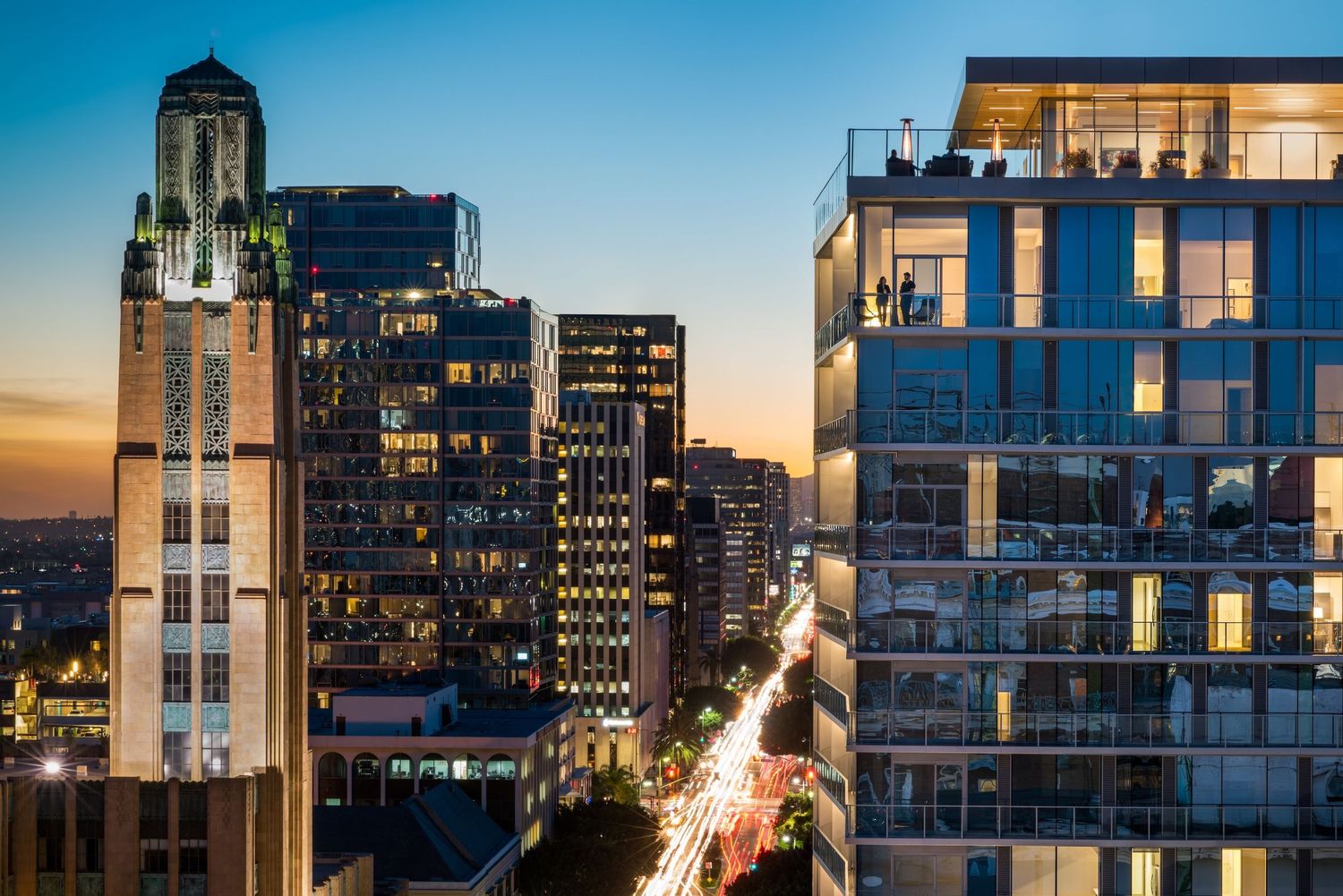 Modern city skyline at dusk with illuminated high-rise buildings and construction cranes.