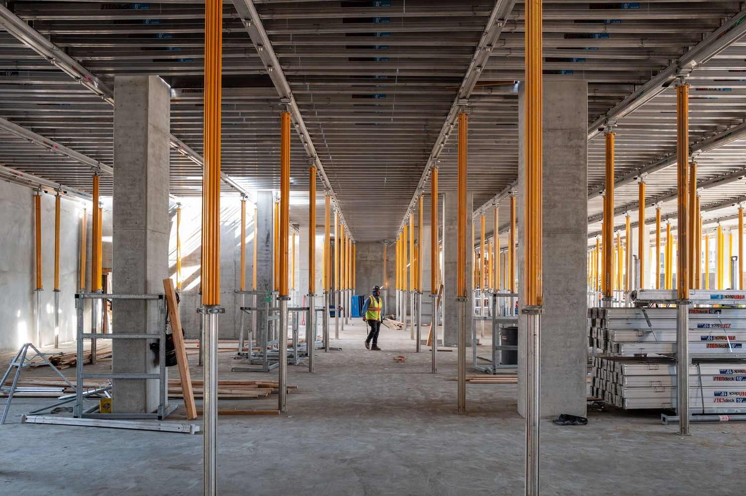 Interior construction site showing concrete pillars and orange support beams.