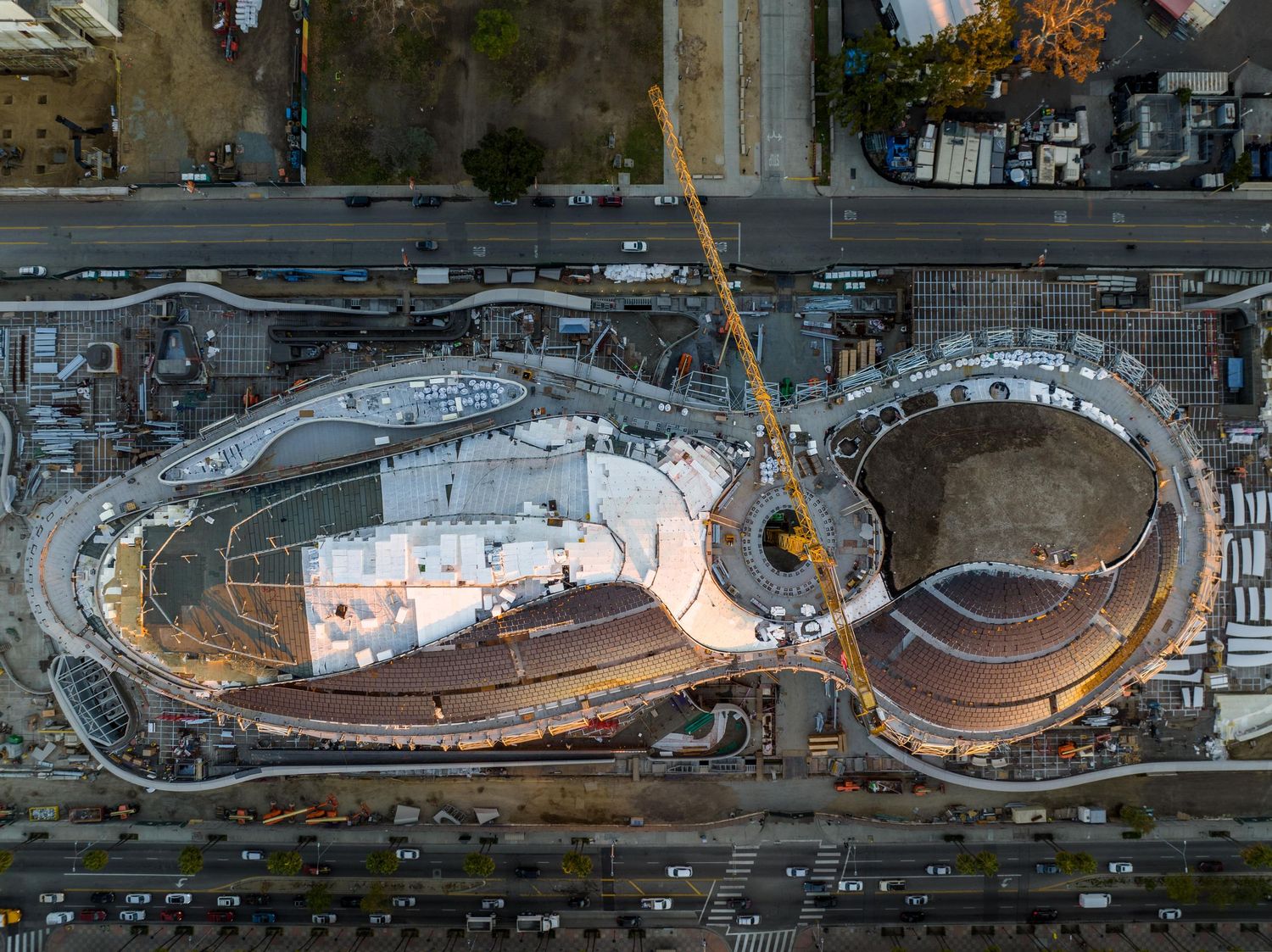 Bird's eye view of a curved building structure under construction with surrounding roadways.