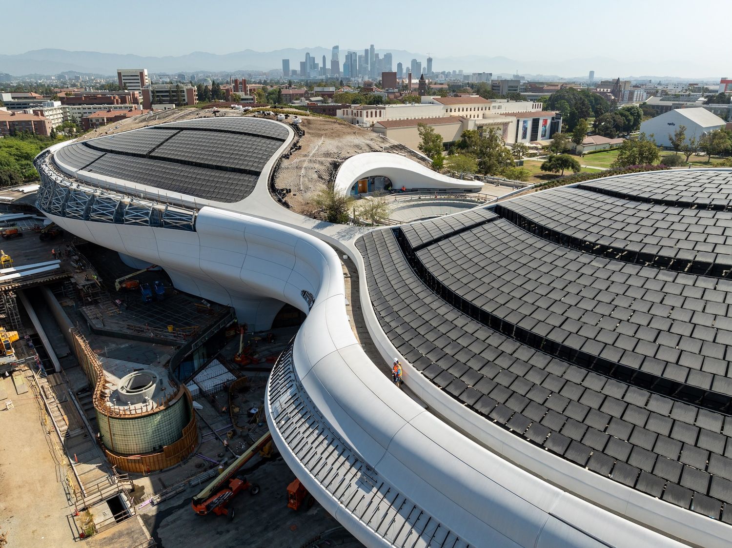 Panoramic shot of stadium construction featuring curved roofline and solar panel installation progress.