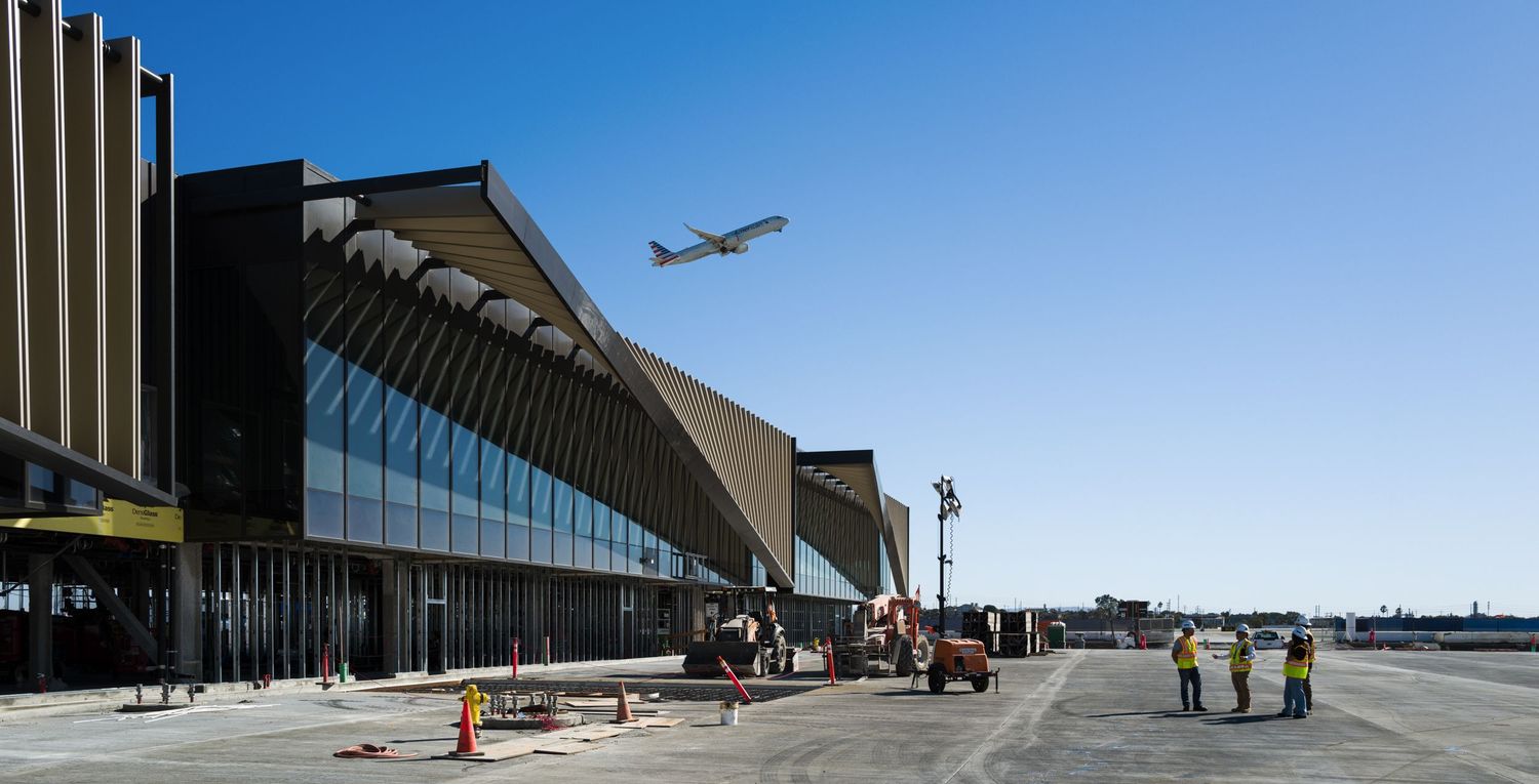 Commercial aircraft flying over modern airport terminal building with glass facade.