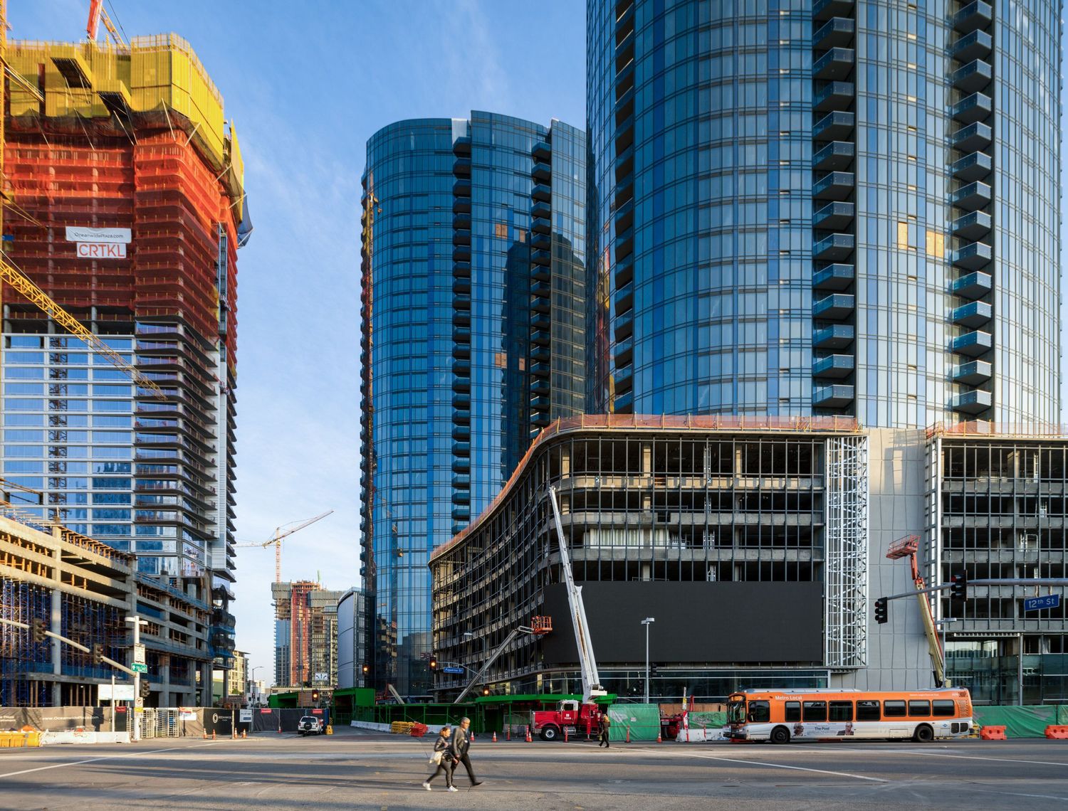 Modern glass office towers and construction sites along urban street with blue sky.