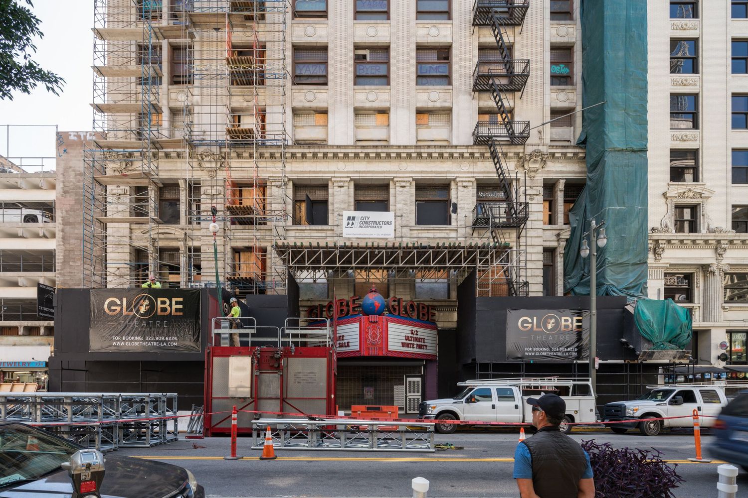 Row of commercial storefronts and retail spaces along an urban street with construction barriers.