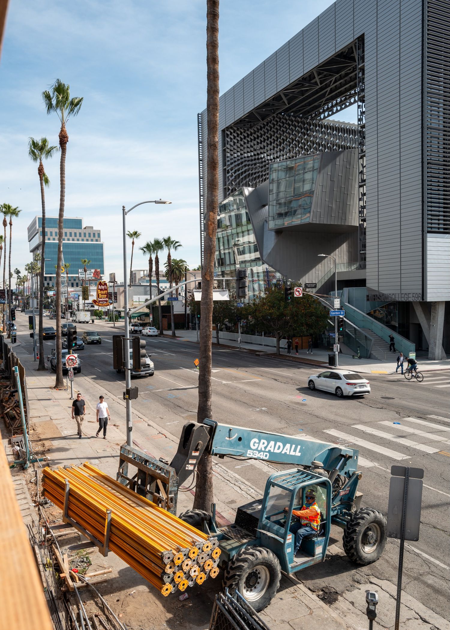 Construction equipment and materials being delivered on a palm tree-lined urban street.