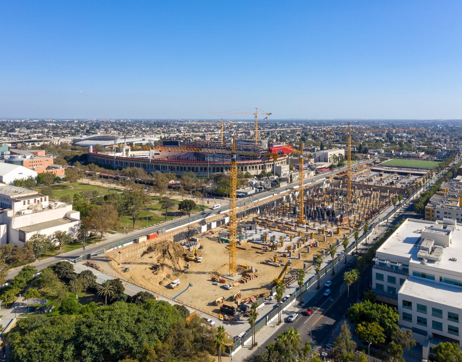 Aerial panorama showing construction progress of a large circular stadium complex with surrounding urban development.