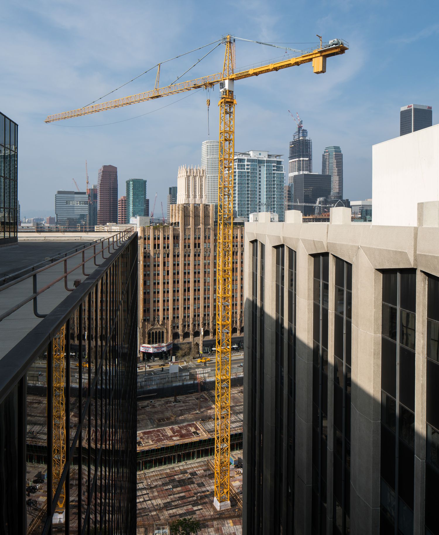 Construction site with yellow cranes against city skyline and blue sky.