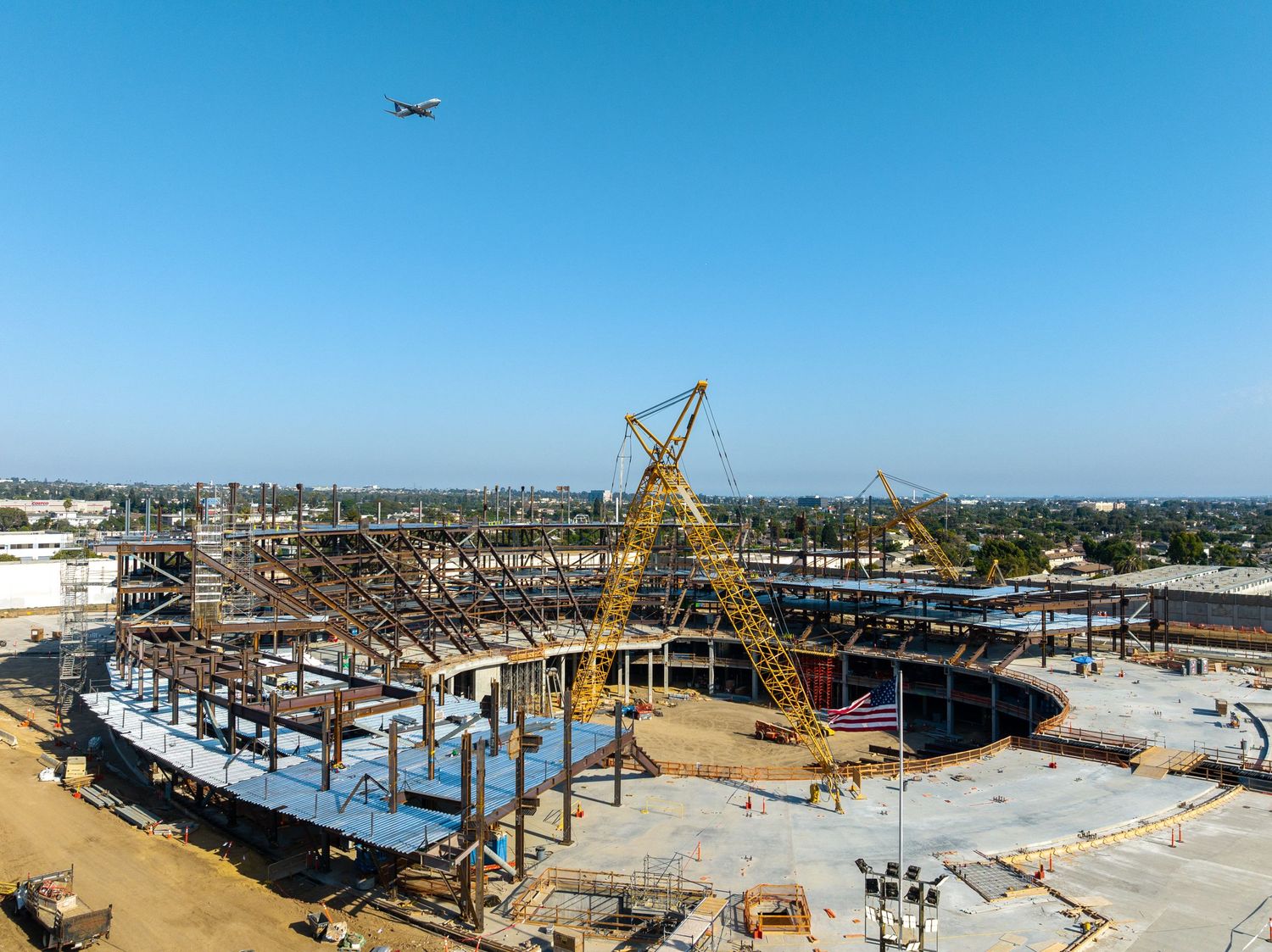 Aerial view of construction site with yellow crane and steel framework against blue sky.