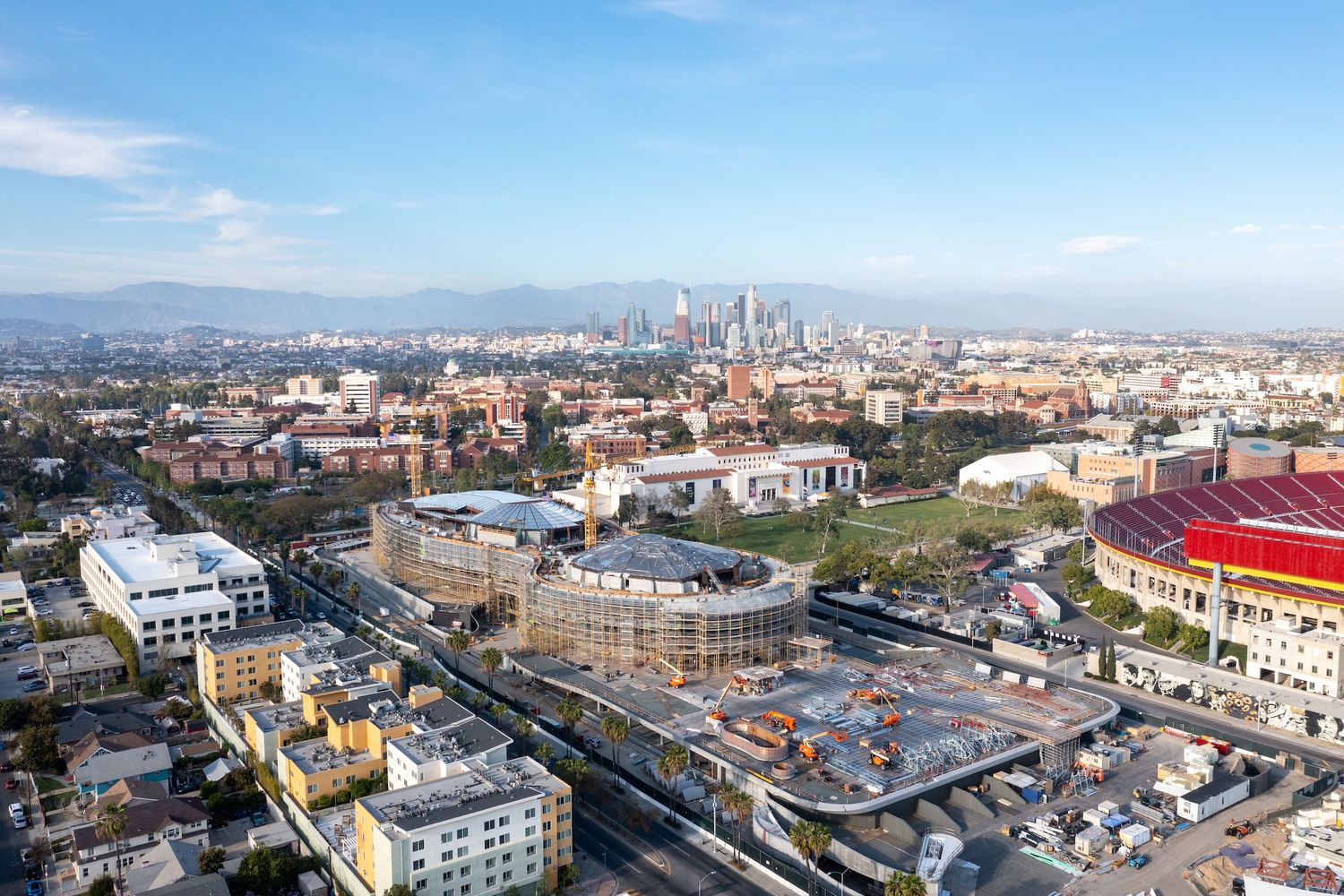 Panoramic cityscape view showing a circular stadium structure under construction amid urban surroundings.