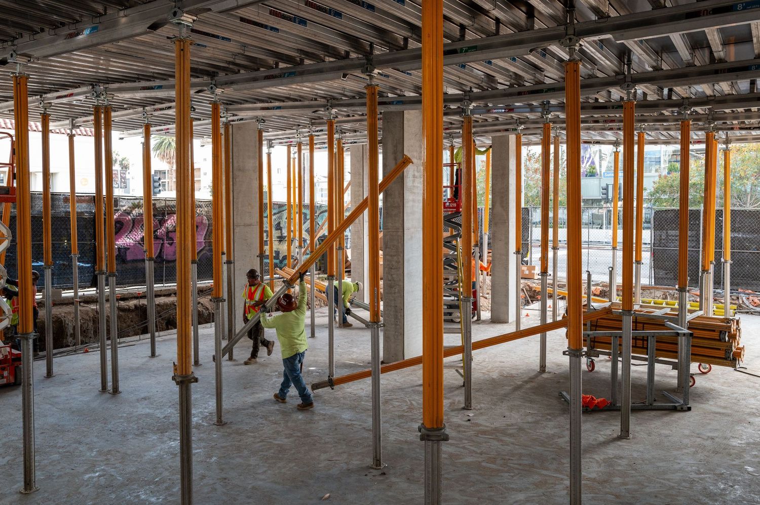 Wide view of construction site interior with orange support posts and exposed ceiling beams.