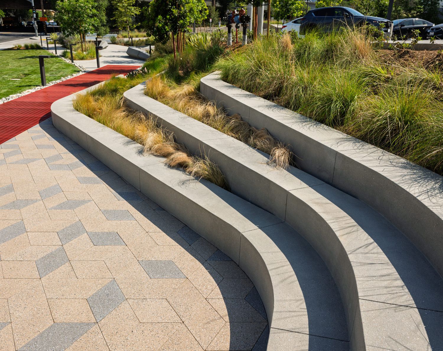 Curved concrete benches with decorative paving stones create a modern outdoor seating area in a landscaped garden setting.