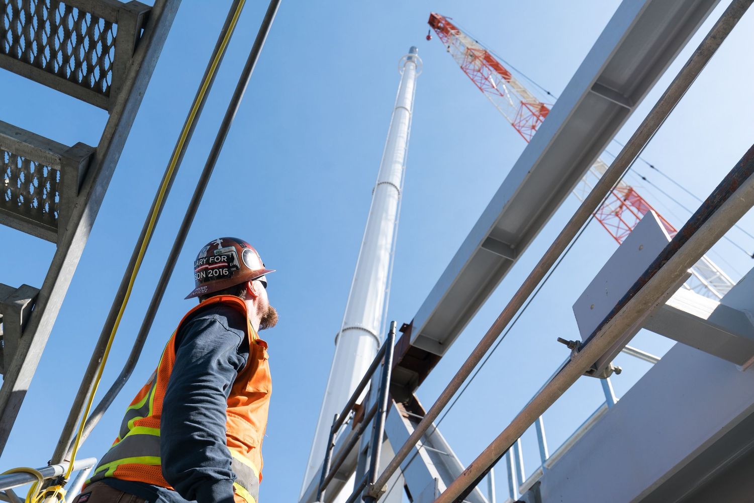 Construction workers on elevated platform with structural beams against blue sky.