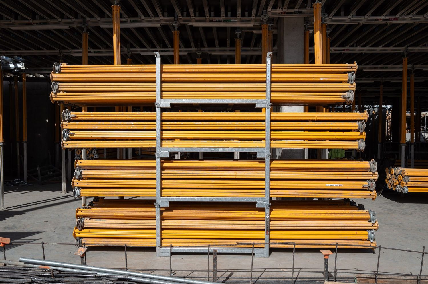 Stacks of yellow metal support beams arranged at a construction site.