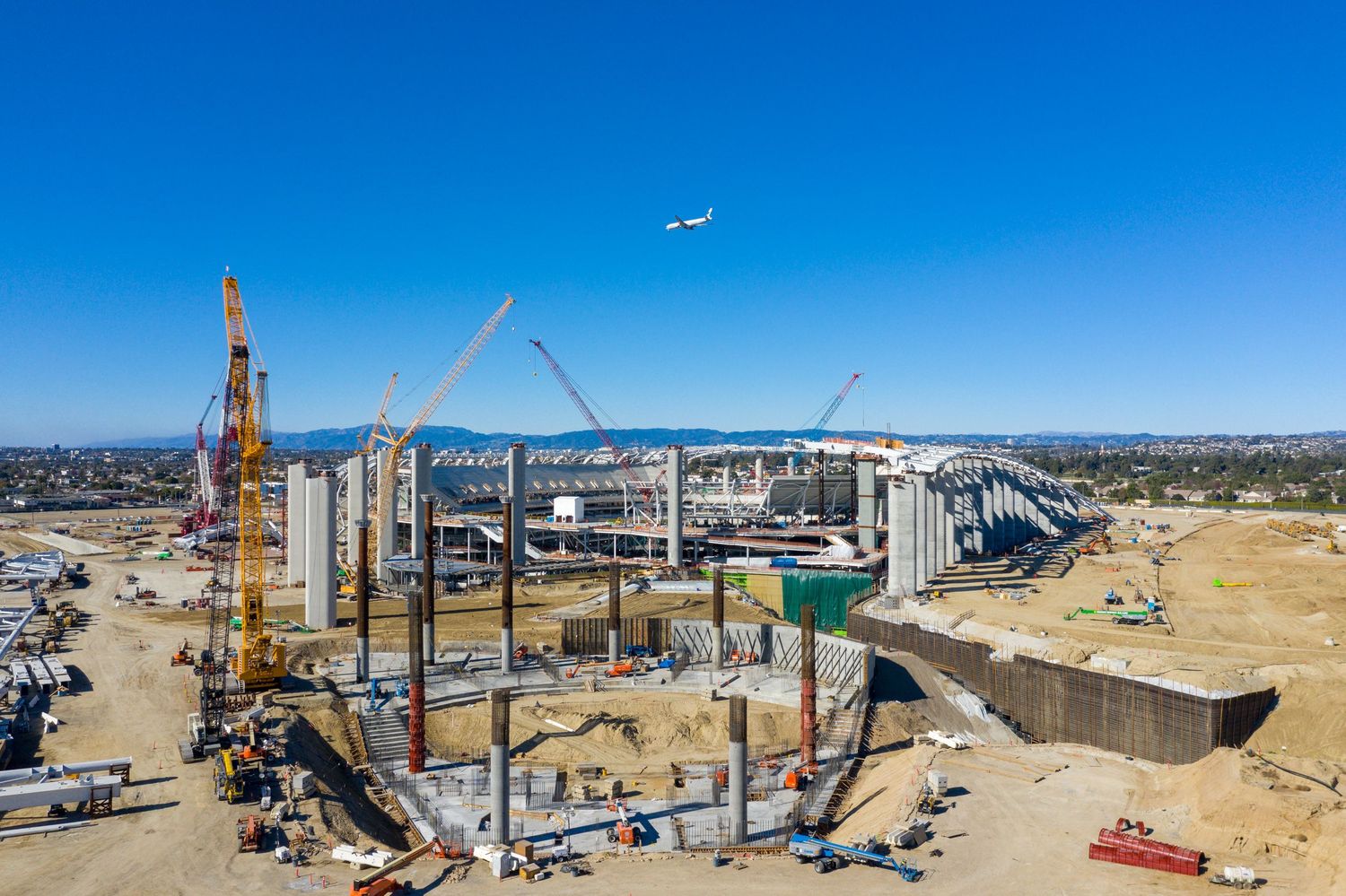 Wide aerial view of an industrial construction site with cranes and equipment near a waterfront.