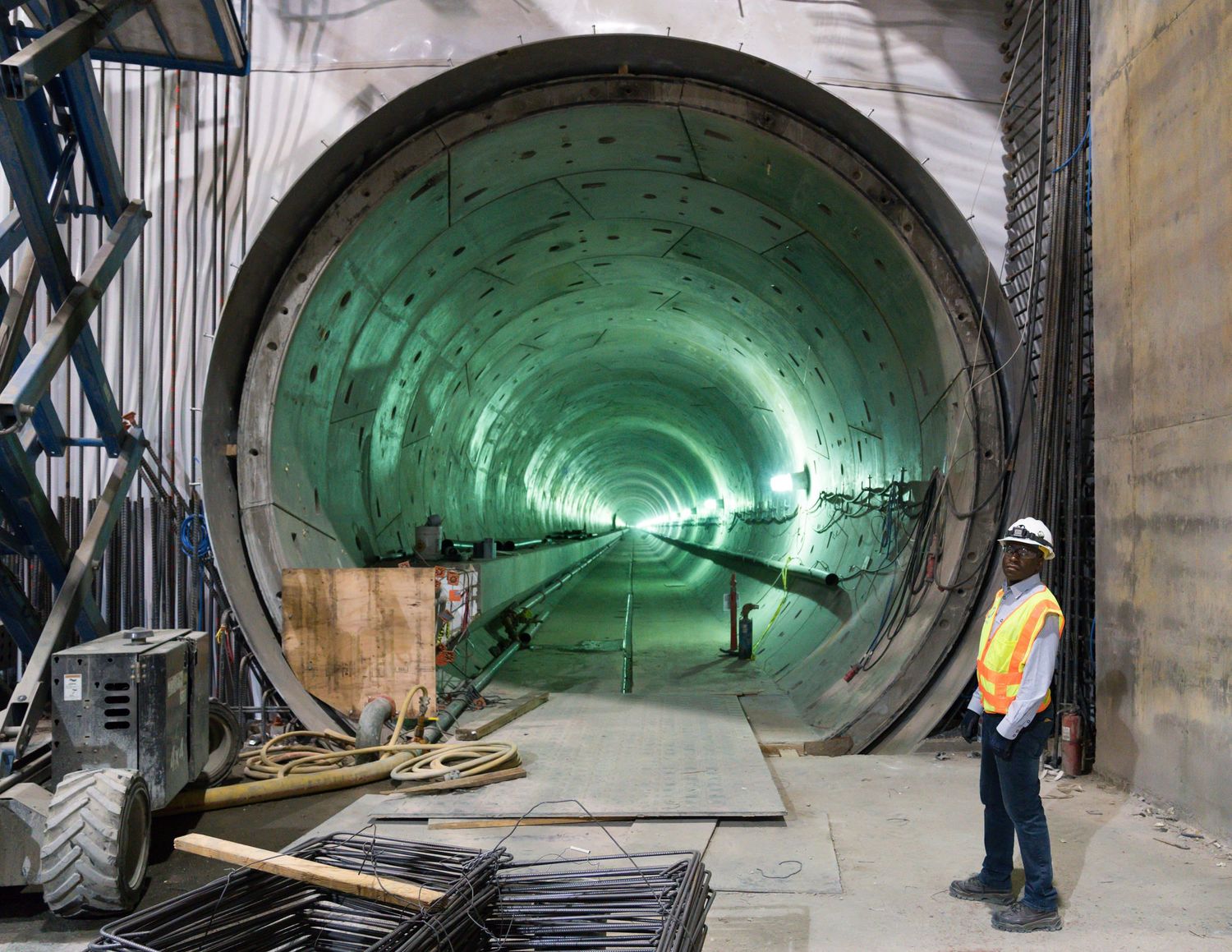 Green-lit tunnel construction site with curved concrete walls and construction equipment.