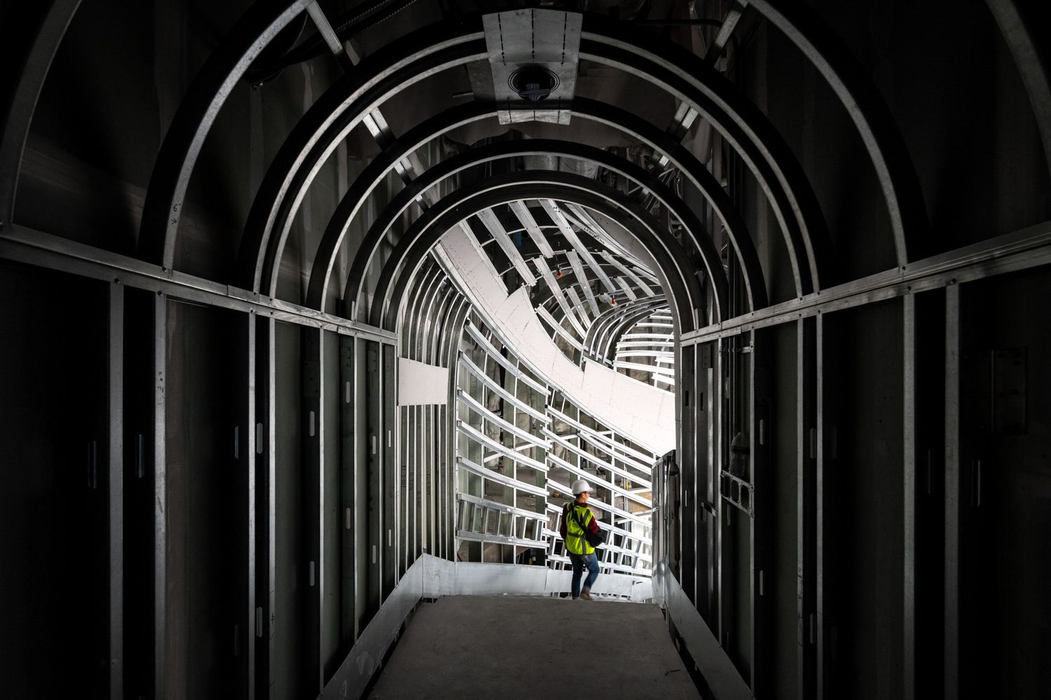 Dramatic black and white photo of figure walking through curved architectural tunnel.