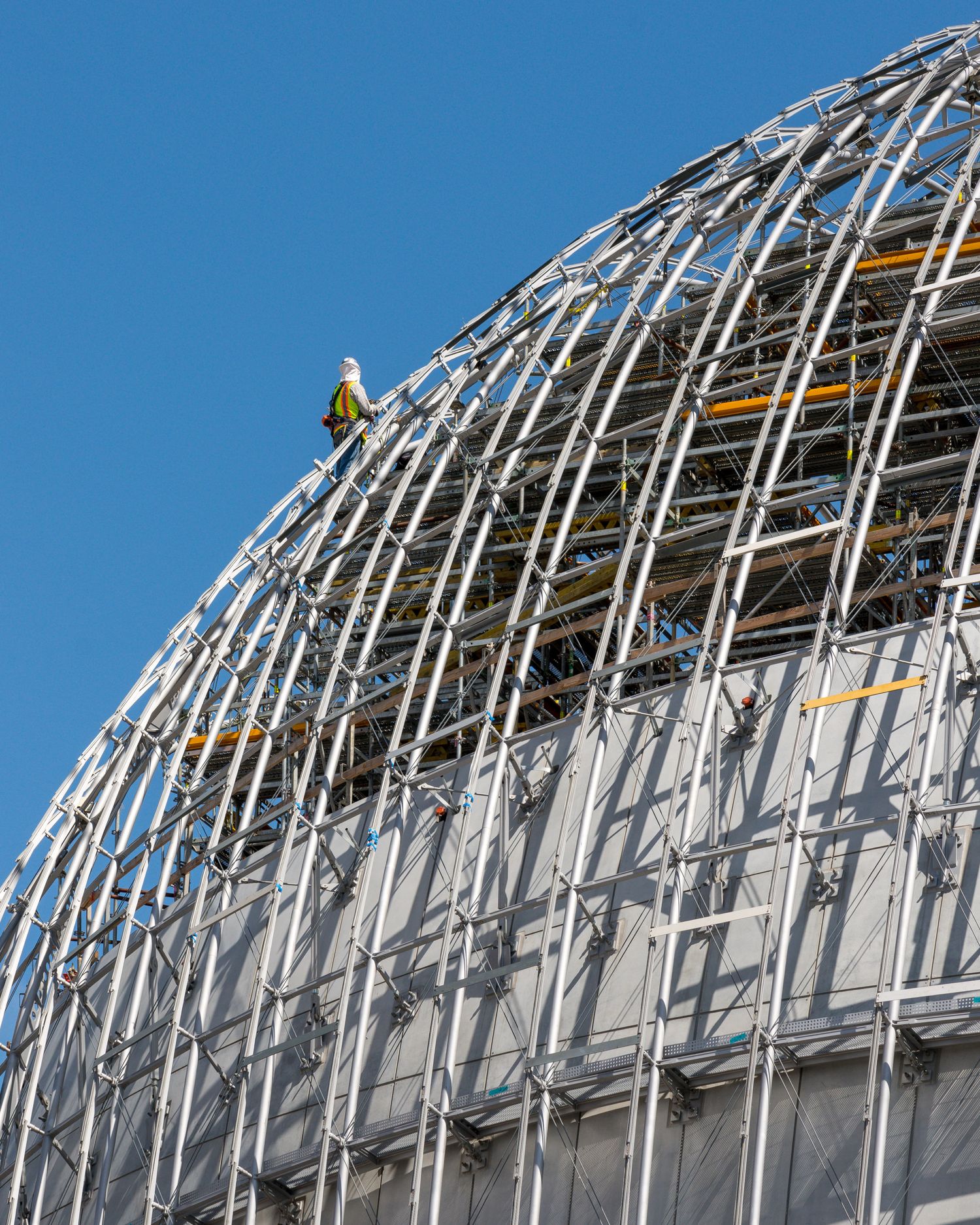 Curved white architectural framework structure against bright blue sky.