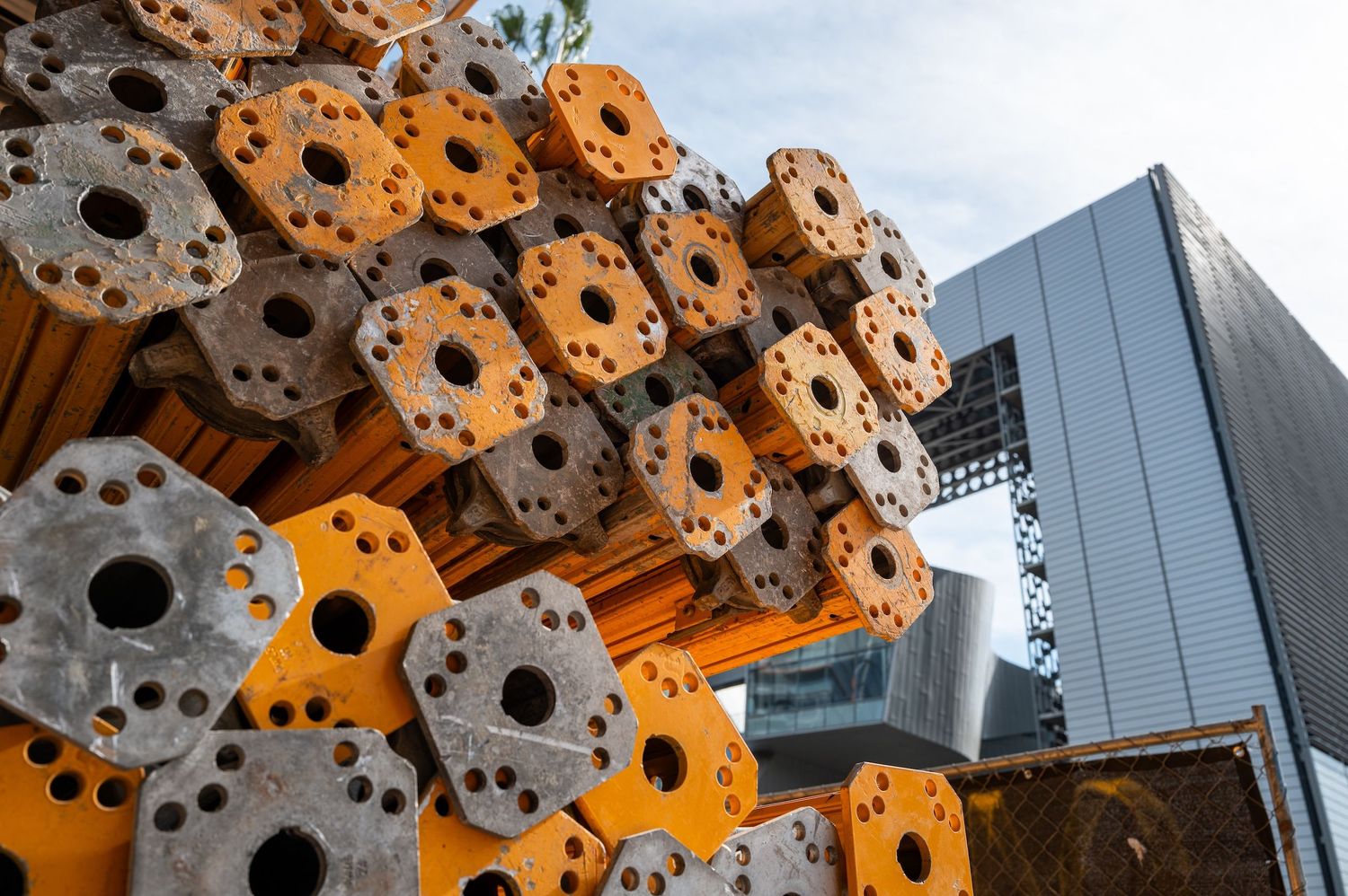 Close-up of orange metal scaffolding components stacked at construction site.