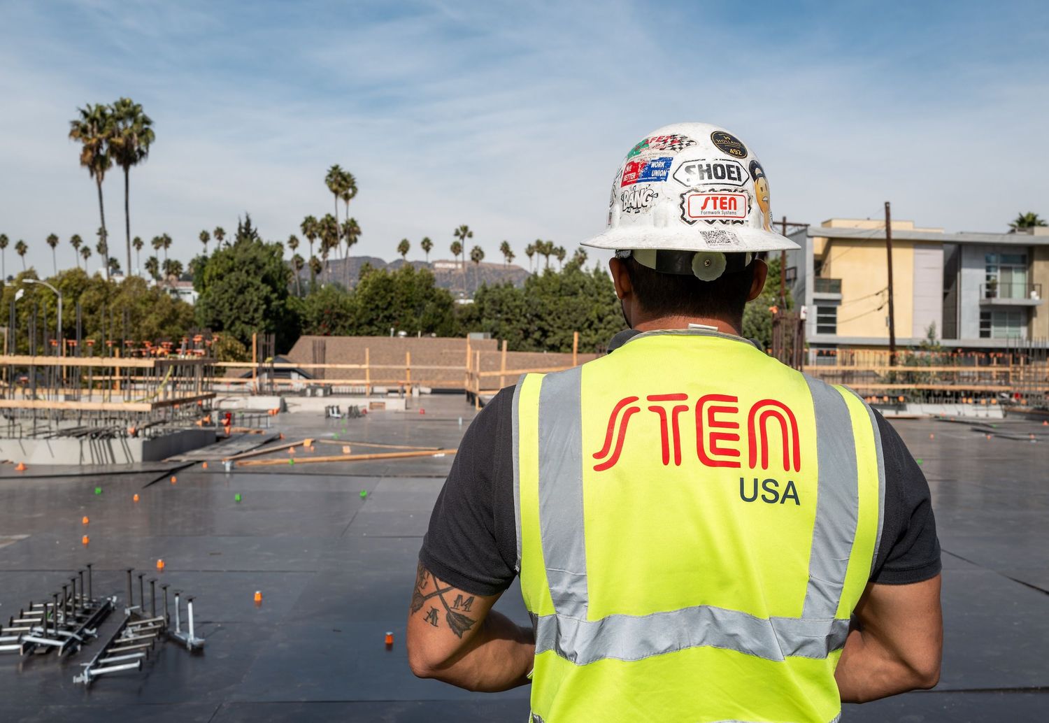 Construction workers in safety vests surveying a commercial building site with palm trees in background.