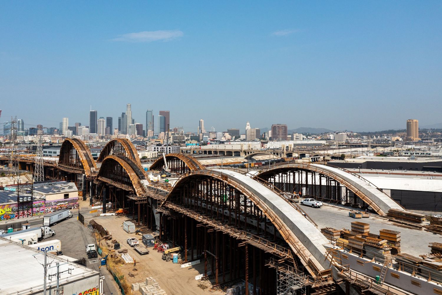 Curved steel arches under construction at a major transit hub with city skyline in background.