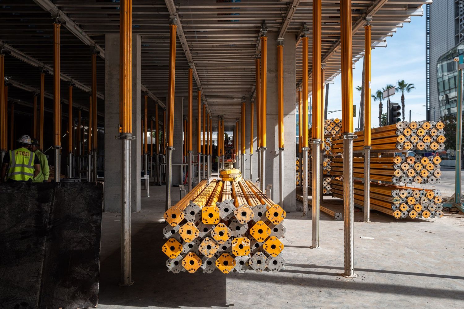 Interior construction site with rows of yellow support posts casting dramatic shadows.