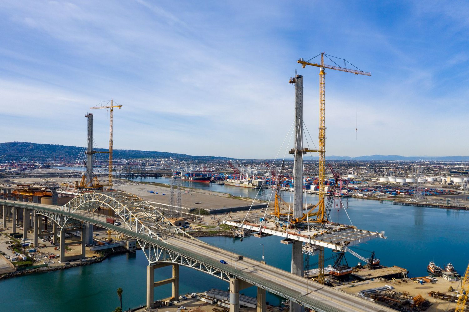 Panoramic view of a harbor construction site with cranes and industrial equipment against blue sky.