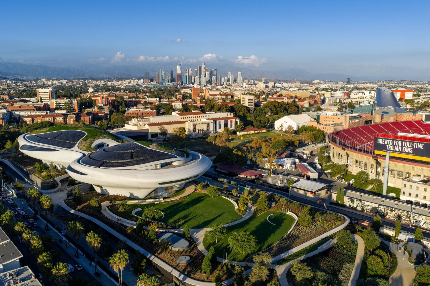 Wide aerial shot of a sports arena with distinctive white curved roof design amid urban landscape.