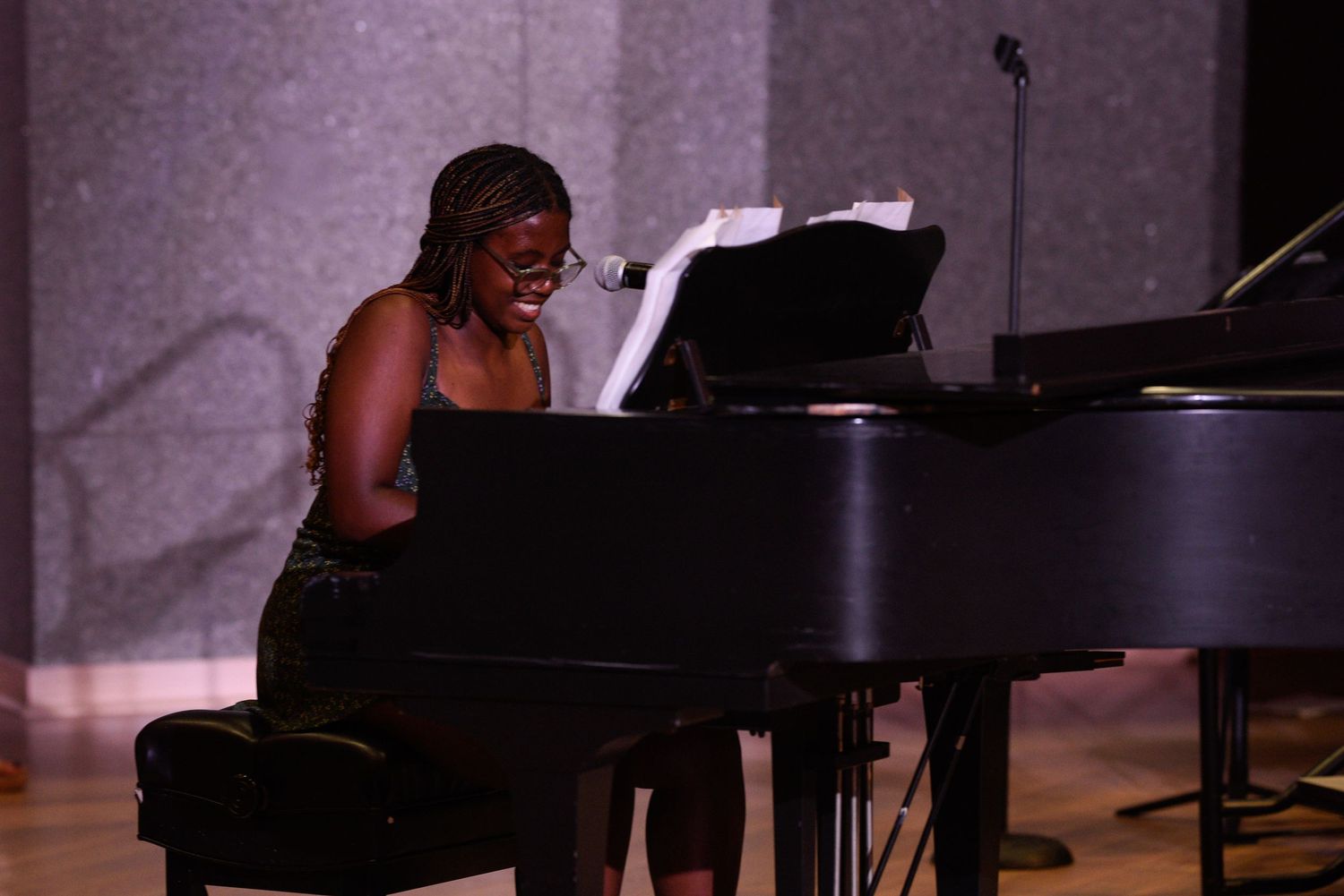 Young woman plays grand piano and sings during a live performance on a concert stage.