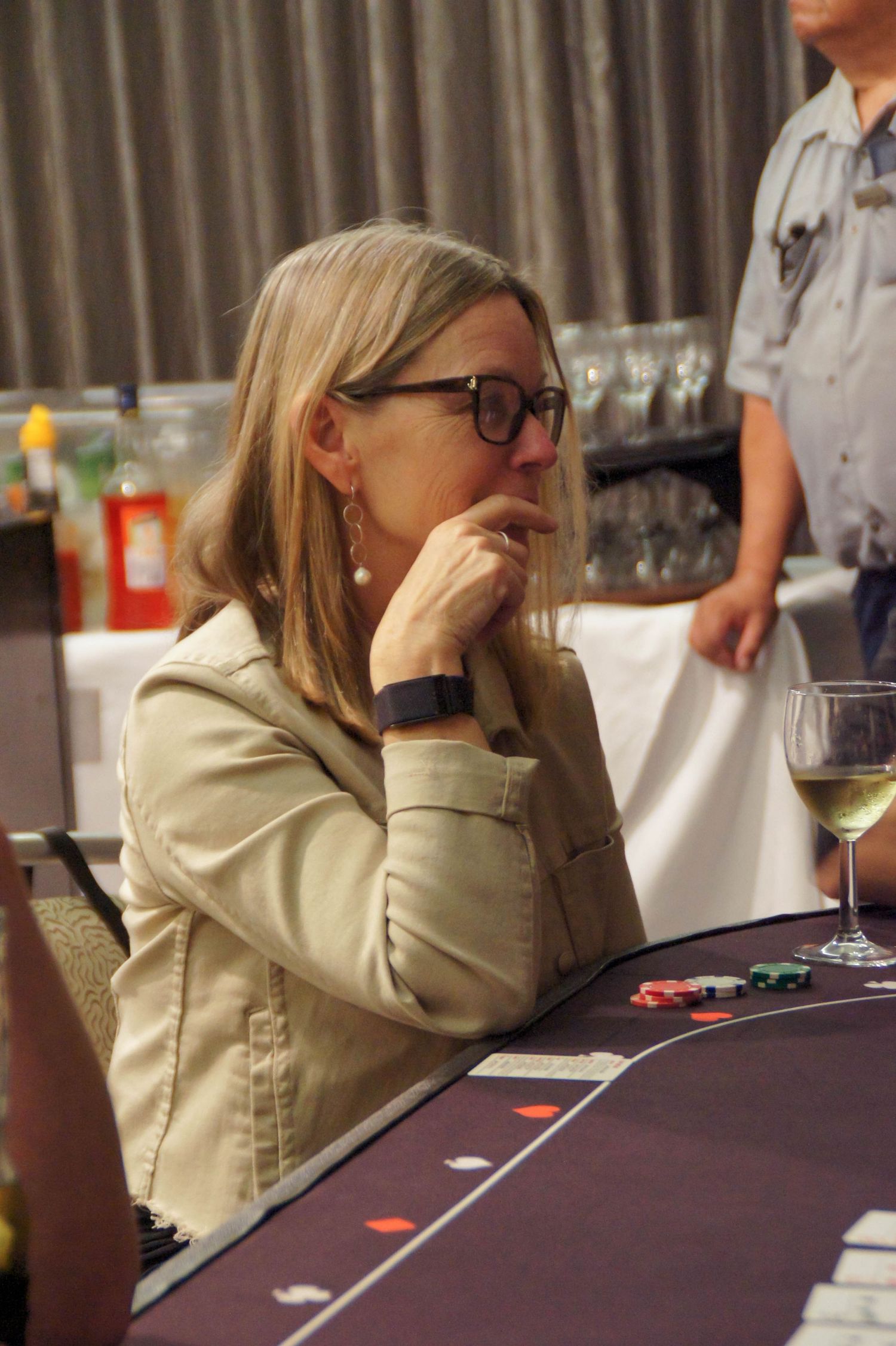 Woman in glasses pensively sitting at a poker table with casino chips.
