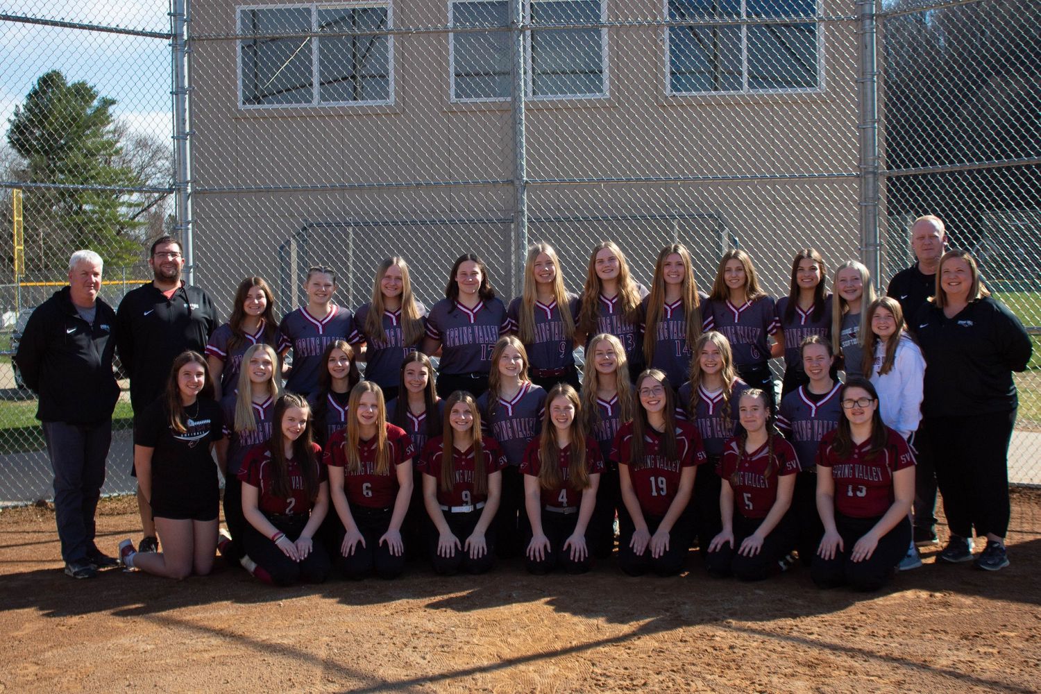 Spring Valley softball team poses for a group photo outdoors on the field in maroon and purple jerseys.