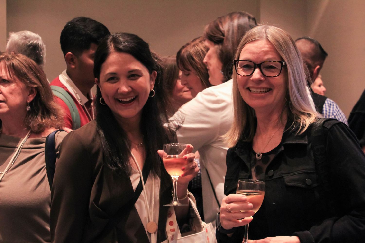 Two smiling women holding cocktails at a social networking event.