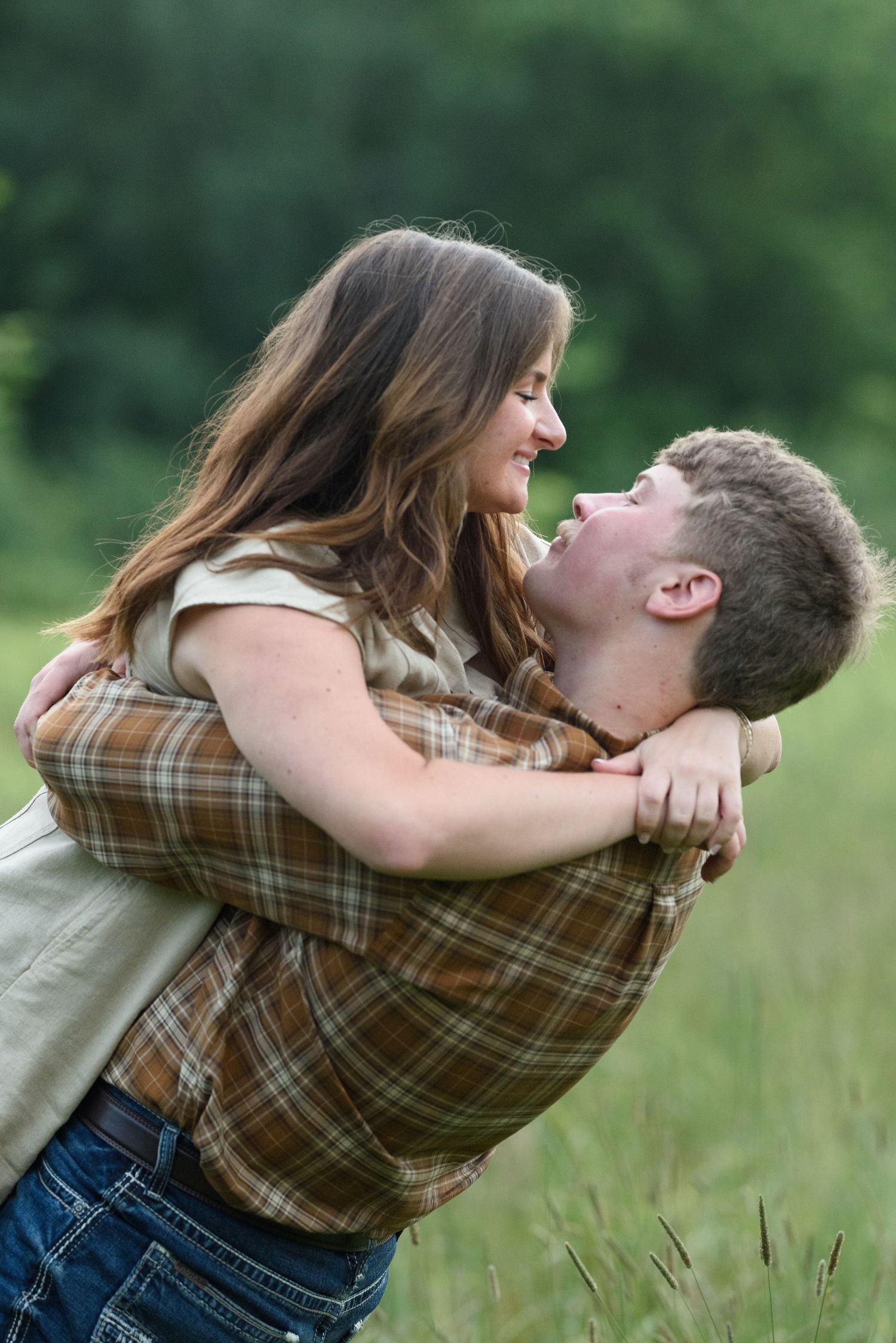 A young couple embracing in a green field, smiling at each other as the man lifts the woman.