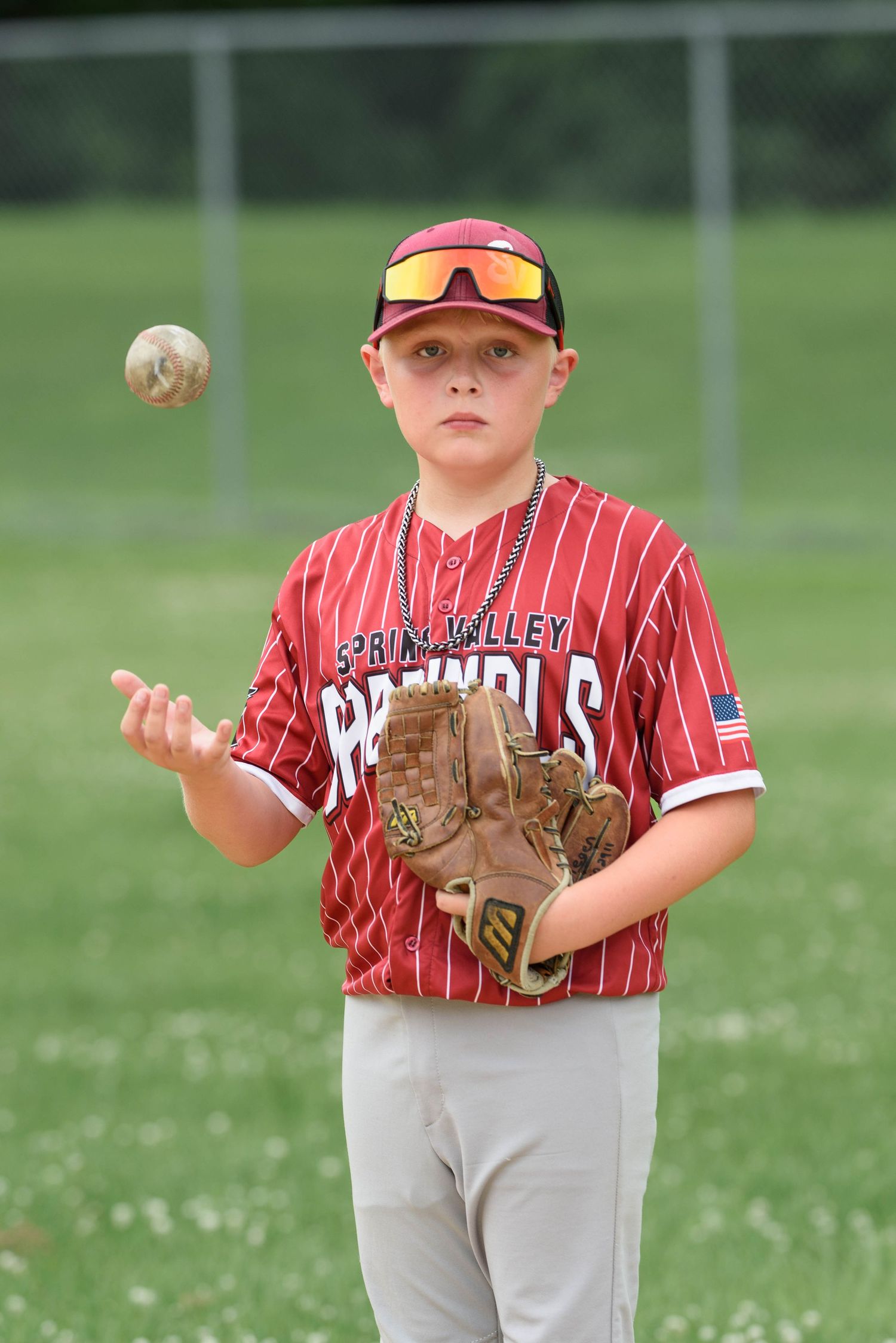 Young baseball player in Spring Valley Cardinals uniform tossing a ball while wearing a glove on a green field.