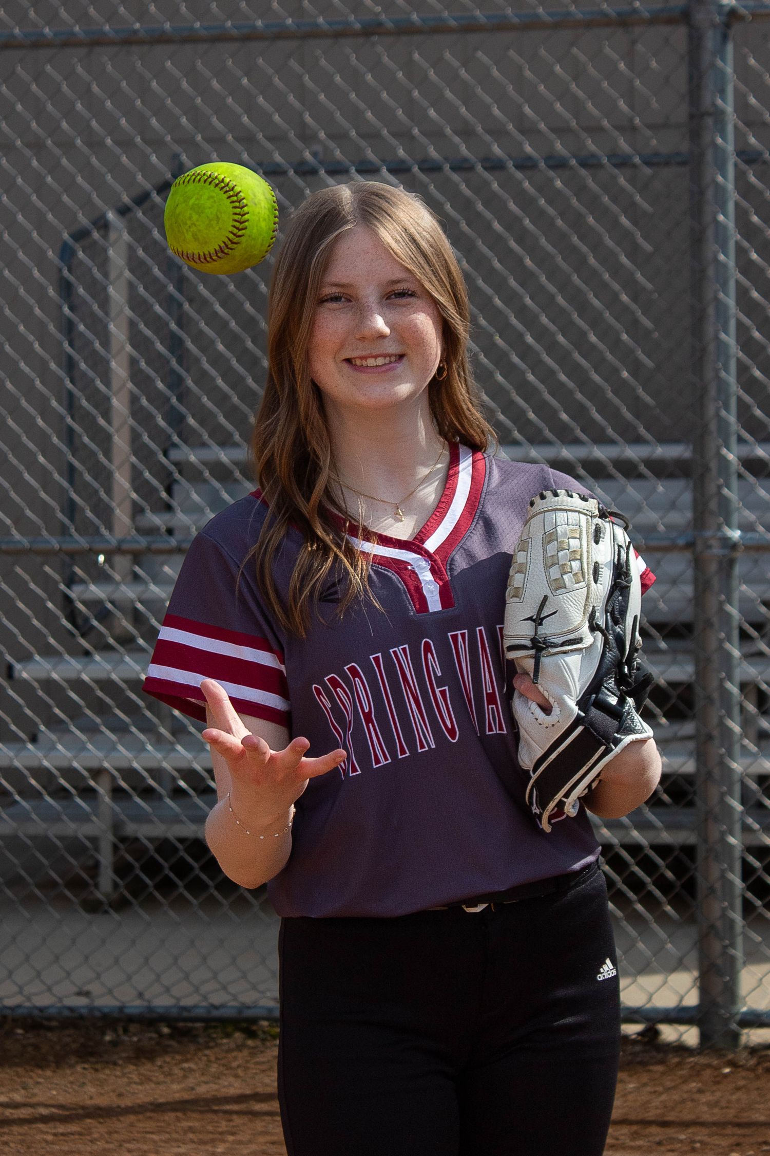Spring Valley softball player tosses a yellow softball in the air while holding a glove outdoors.