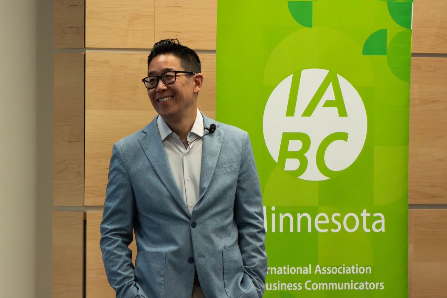 Man smiling in blue blazer standing next to IABC Minnesota International Association of Business Communicators banner.