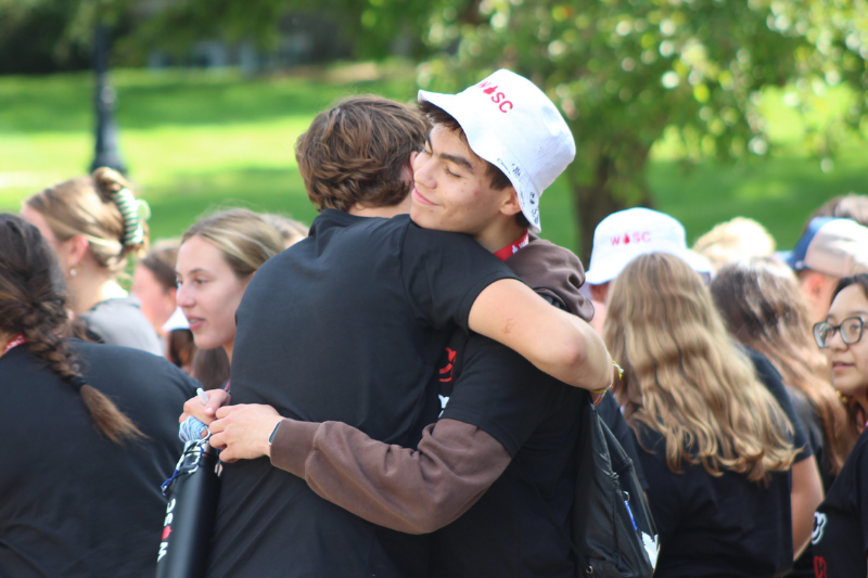 Two students share a warm hug outdoors during a school or camp farewell gathering.