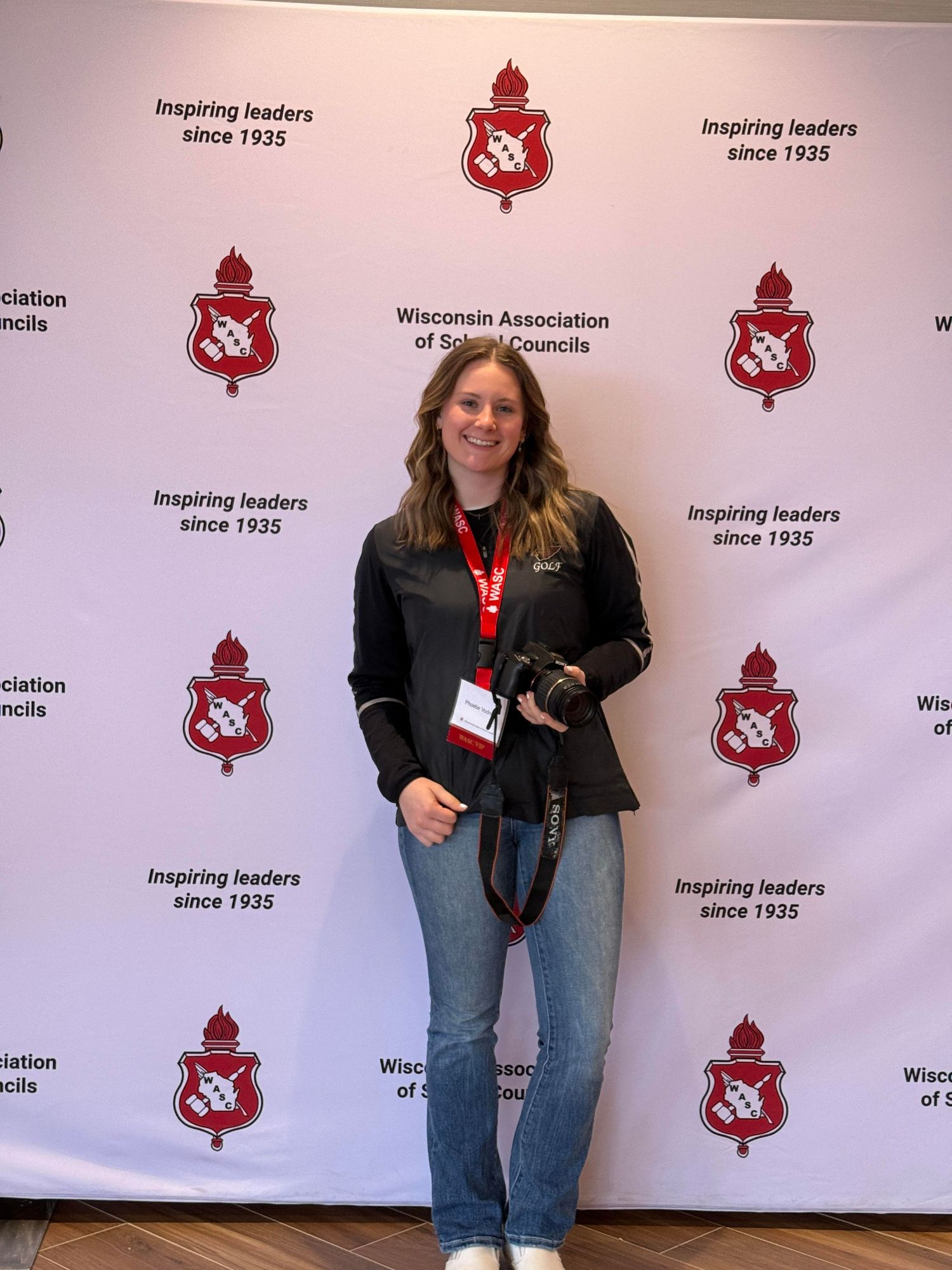 Student poses with camera at Wisconsin Association of School Councils conference backdrop.